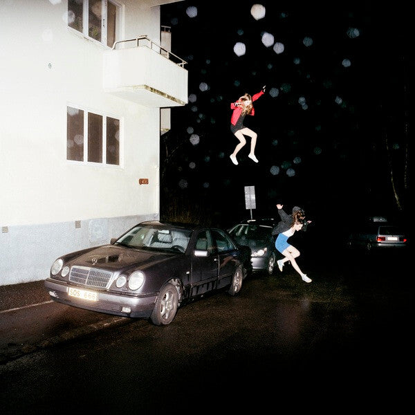 Two people in costumes leaping in the air over a car on a dark street.