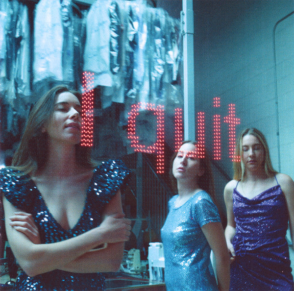 Three women in sequin dresses standing in front of a 'I Quit' sign.