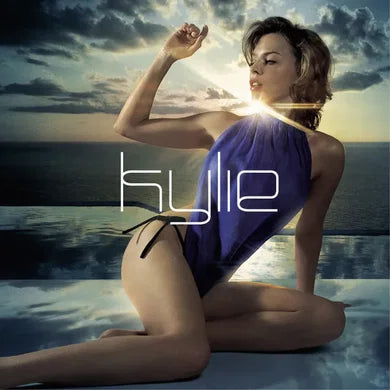 Cover art for Light Years by Kylie. Features a photo of Kylie wearing a royal blue bodysuit sitting on the edge of an infinity pool next to the ocean with sunbeams shining next to kylies face. 