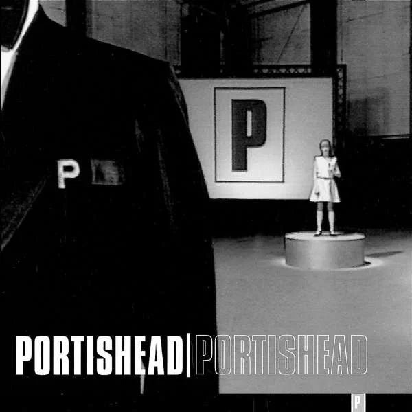 Cover art for Portishead's self titled record. Shows a cropped image of a man in a tuxedo with a embroidered P in the foreground  and a women in a white dress standing on plinth in the background. A large  is displayed on a screen behind the women. 